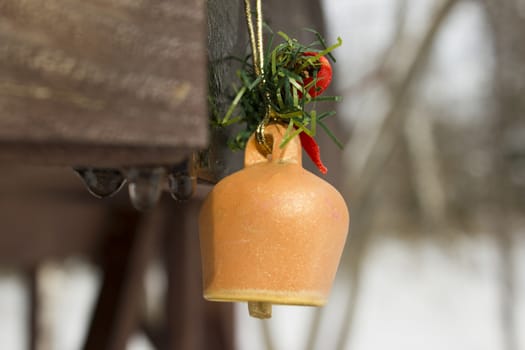 Toy bell pinned on a wooden frame with melting snow water drops running down.