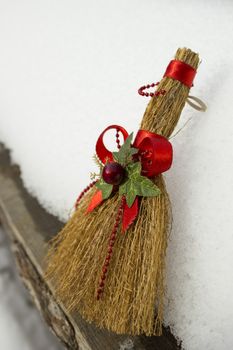 Toy broom with red ribbon and holiday ornaments laying around the snow.