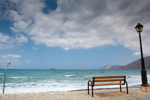 A bench, a lantern and a public shower on an empty beach in Crete. The weather will become soon bad wit heavy clouds in the sky