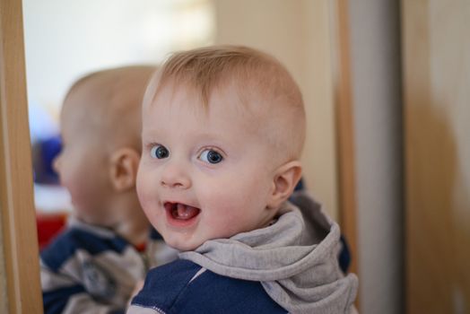 Portrait of a eight month old baby boy in front of a mirror looking curious at the camera