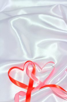 Red and pink satin glossy ribbon hearts over white silk background