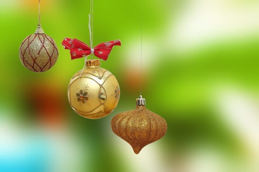 three gold christmas baubles on green out of focus background