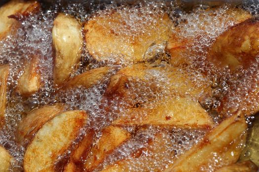 Potato wedges or chips deep frying in a pan of oil 