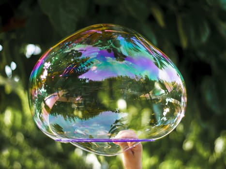 Hand of a child holding a hoop with a big soap bubble