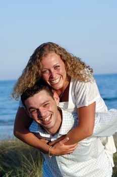 A happy woman and man in love at beach. The young man is carrying his girlfriend on the back of his shoulders.