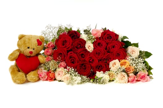 Bouquet of rose flowers isolated on white background. The roses are aranged as a heart shape. A teddy bear is sitting next to the heart.