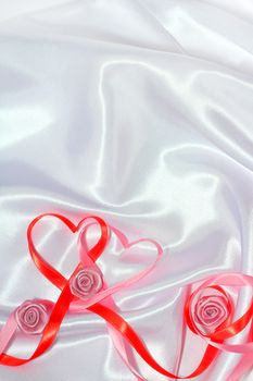 Red and pink satin glossy ribbon hearts and roses over white silk background