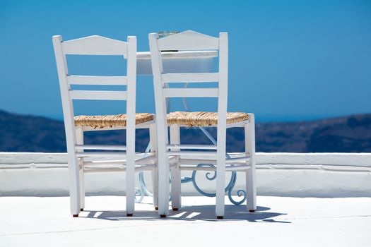 Two white chairs and a blurred panoramic view of the hills of santorini, Greece 2013.