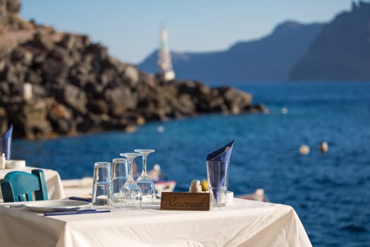 Reserved table in front of the aegean sea, in the blurred background , you see the shore-line of Santorini.