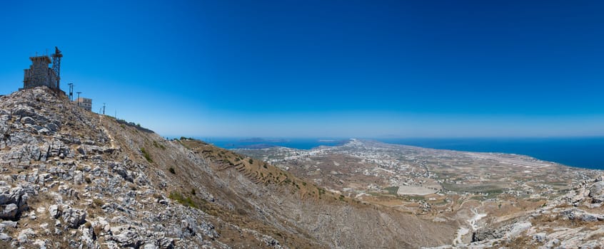 Communication tower on a hill and a panorama of Santorini island with a clear blue sky going up in the sea, Greece.