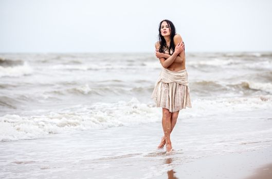 Beautiful young seminude woman in the cold sea waves