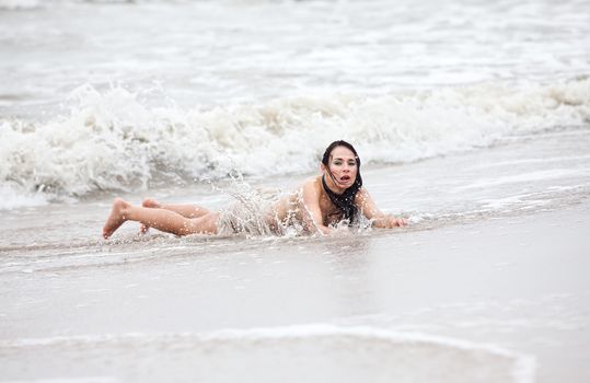 Beautiful young seminude woman in the cold sea waves