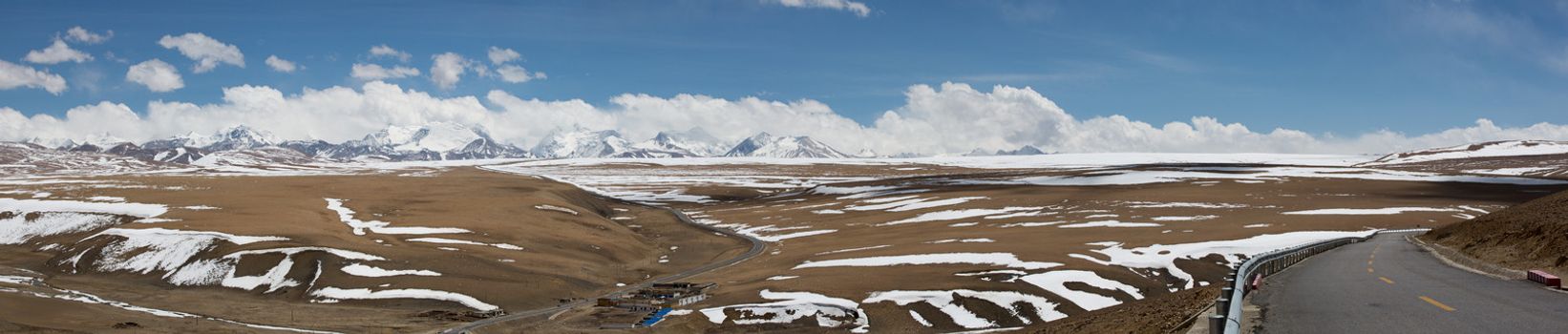 Panoramic view of the road with Tibetan landscape of Mountains in the background. There is s mall village in the foreground. The great Himalayas mountain range is the background. Friendship Highway, Tibet. China 2013