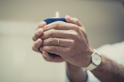 Hands protecting a blue candle over white