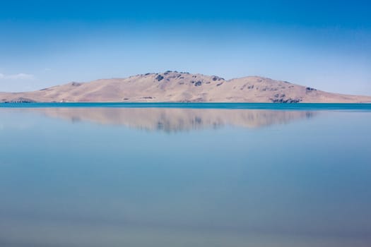 Peace full lake and a small mountain with its reflection in it. A clear blue sky in the background on the Tibetan Plateau in China. 2013.