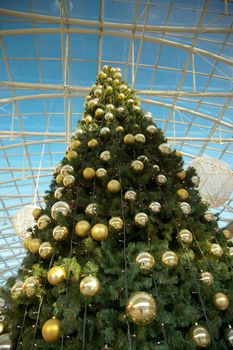 A decorated Christmas tree sitting in front of an open door in a shopping mall with yellow balls