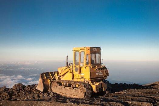 Blue sky with Yellow tractor at the top of the Etna mountain with view on the clouds and the valley