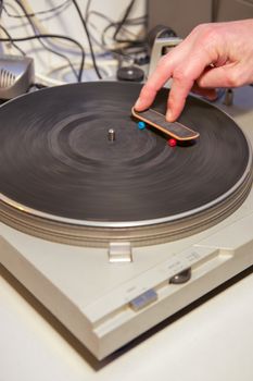 Two fingers holding a small skateboard turing on a vintage turntable