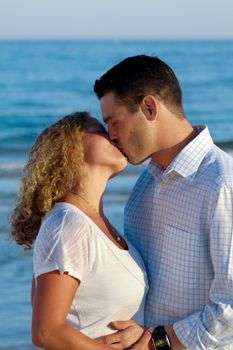 A young couple a standing near beach kissing.