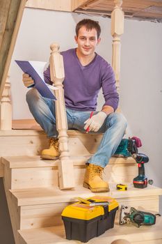 young carpenter sitting on step of of ladder with tools
