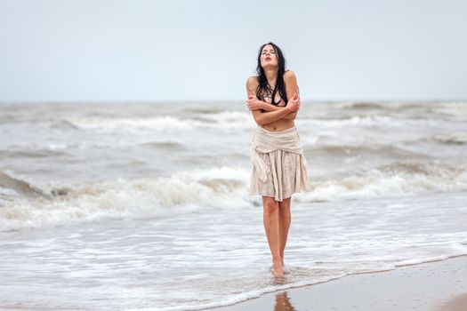 Beautiful young seminude woman in the cold sea waves