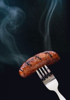 Steaming hot sausage on a fork over a black background