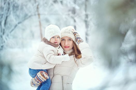 Young mother holding a daughter in a winter forest for a walk