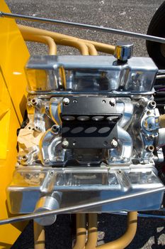 A hotrod engine with a supercharger and multiple air intakes mounted on a yellow frame at bonneville Salt Flats, Utah.