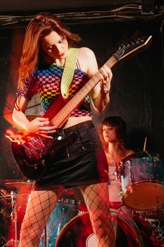 Photo of young beautiful woman playing guitar with drummer in the background.  Motion blur and light trails from slow shutter speed and strobes.