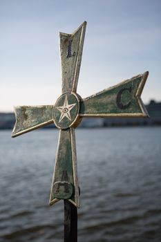 A metallic nordic cross photographed from a low angle against a blue sky with the harbor in the background