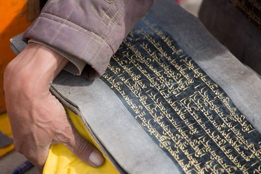 Close-up of a hand carrying a few old and holy Tibetan scripts. The sheet of old peer are protected with a yellow fabric