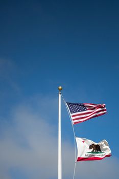 US and california flag state fluttering in the wind against a blue sky