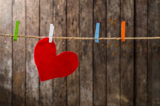 Cute big red heart hanging on the clothesline. On old wood background.