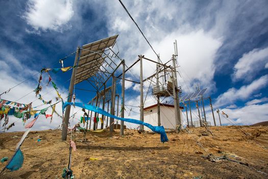 Telecomunication instalation at the top of a mountain in Tibet with prayer fabrics under a blue sky.