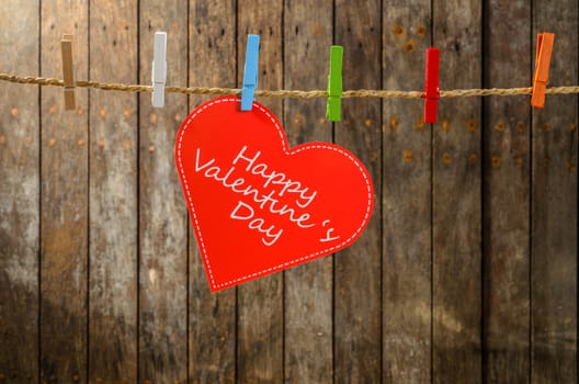 Cute big red heart hanging on the clothesline. On old wood background.