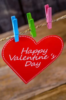 Cute big red heart hanging on the clothesline. On old wood background.