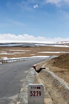 Friendship Highway in Tibet with the view of the mountains and the road, a sign aroad says that we are at 5279 km away from Shanghai