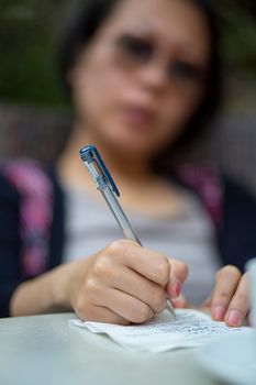 Close-up of an unrecogniable Chinese woman wearing sun glasses and writing a letter on a table in Shanghai. The focus is made on the pen and the hands.