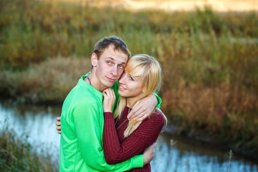 Young couple tenderly and lovingly embrace each other on banks of river