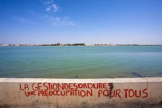 Managing dirts is our problem message written on a small wall with the Senegal River in the background.