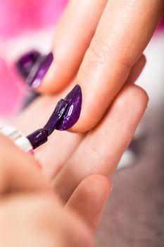 Woman having a nail manicure in a beauty salon with a closeup view of a beautician applying rich purple nail varnish with an applicator