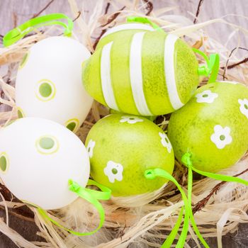 Collection of four hand decorated colourful green Easter eggs with different patterns displayed in straw, close up view