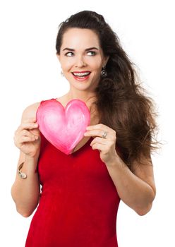A beautiful smiling woman in a red dress holding a red love heart and looking away at copyspace. Isolated on white.