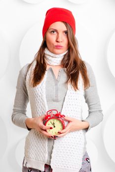 girl in a hat and scarf with red alarm clock