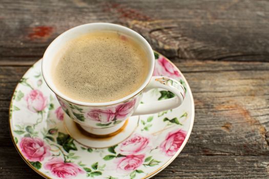 Cup of freshly brewed Turkish coffee in a pretty floral china cup and saucer for a refreshing coffee break, closeup view on a grunge wooden background with copyspace