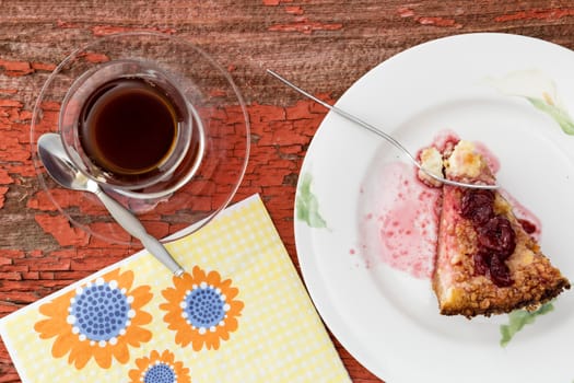 Closeup overhead view of a mug of Turkish tea with freshly baked cheesecake and a pretty floral napkin on an old grungy wood surface with peeling paint
