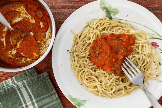 Overhead view of a bowl of tomato based Bolognese sauce and a serving of spaghetti pasta with sauce on a plate alongside