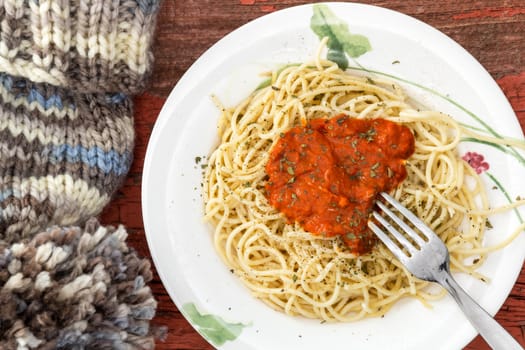 Overhead view of a plate of Italian spaghetti and Bolognese sauce with a knitted woollen winter hat