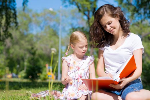 girl with the teacher reading a book together in the summer park