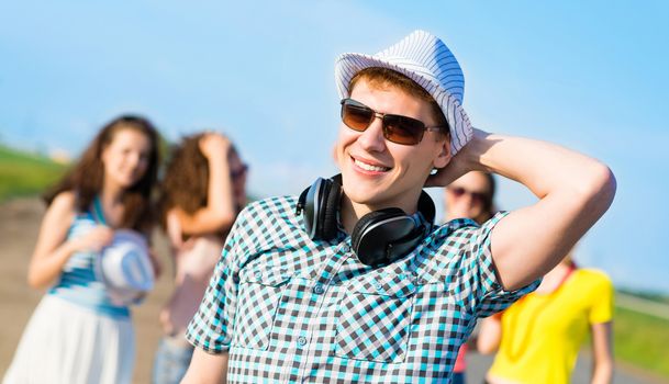 young man in sunglasses, a hat holds a hand on a background of blue sky and friends